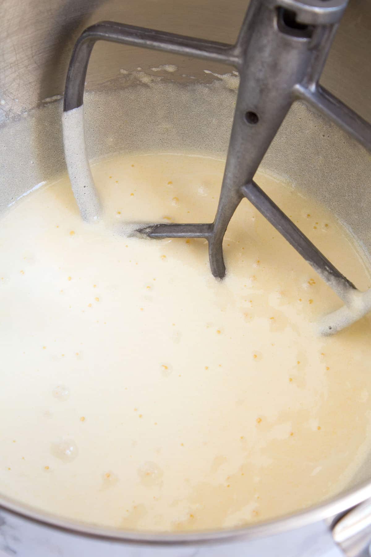 Yellow cake batter in a mixing bowl with a silver paddle attachment sitting in the bowl.