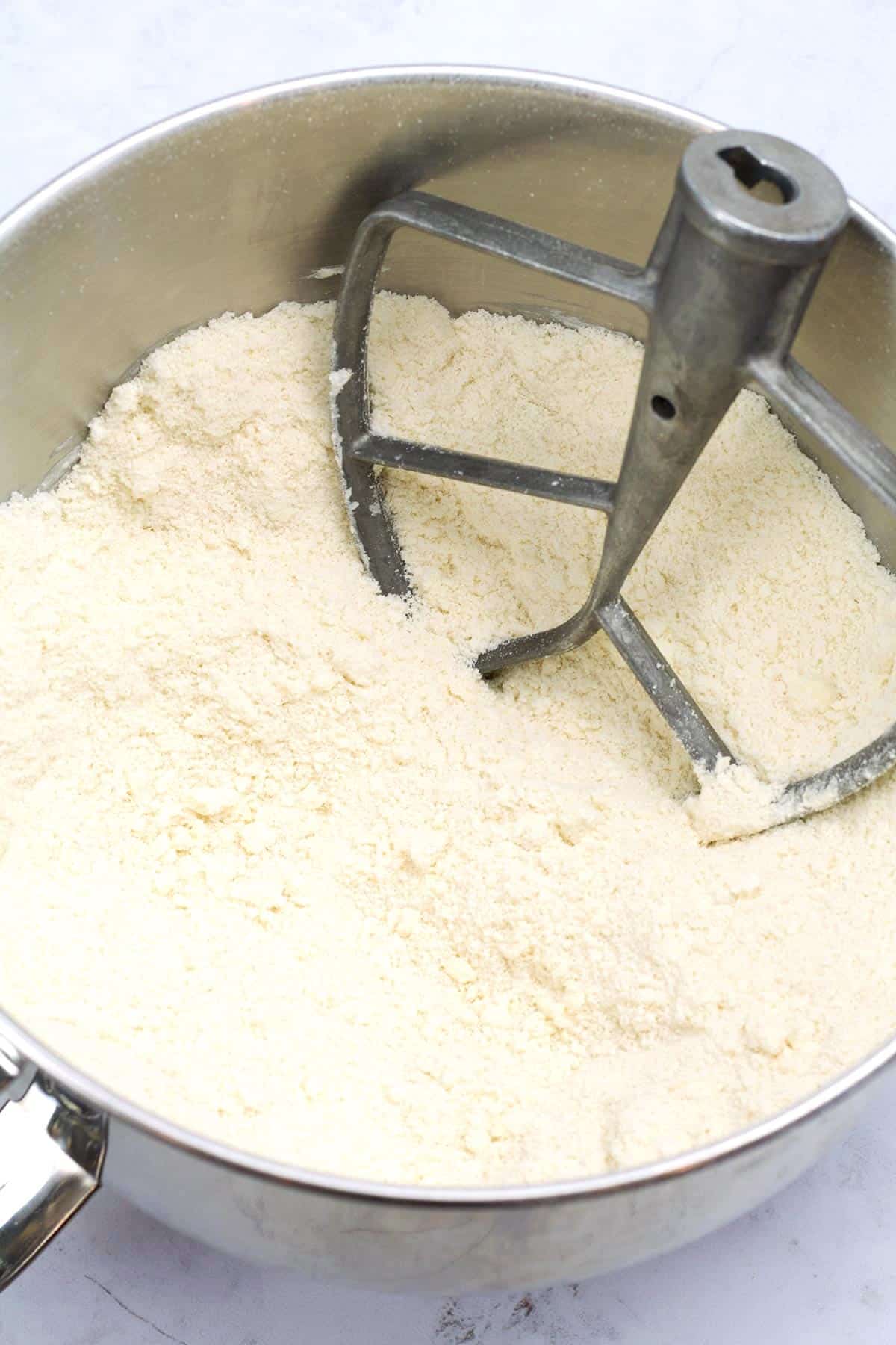 A dry, crumbly flour mixture in a silver mixing bowl with a paddle attachment sitting in the back right side of the bowl.
