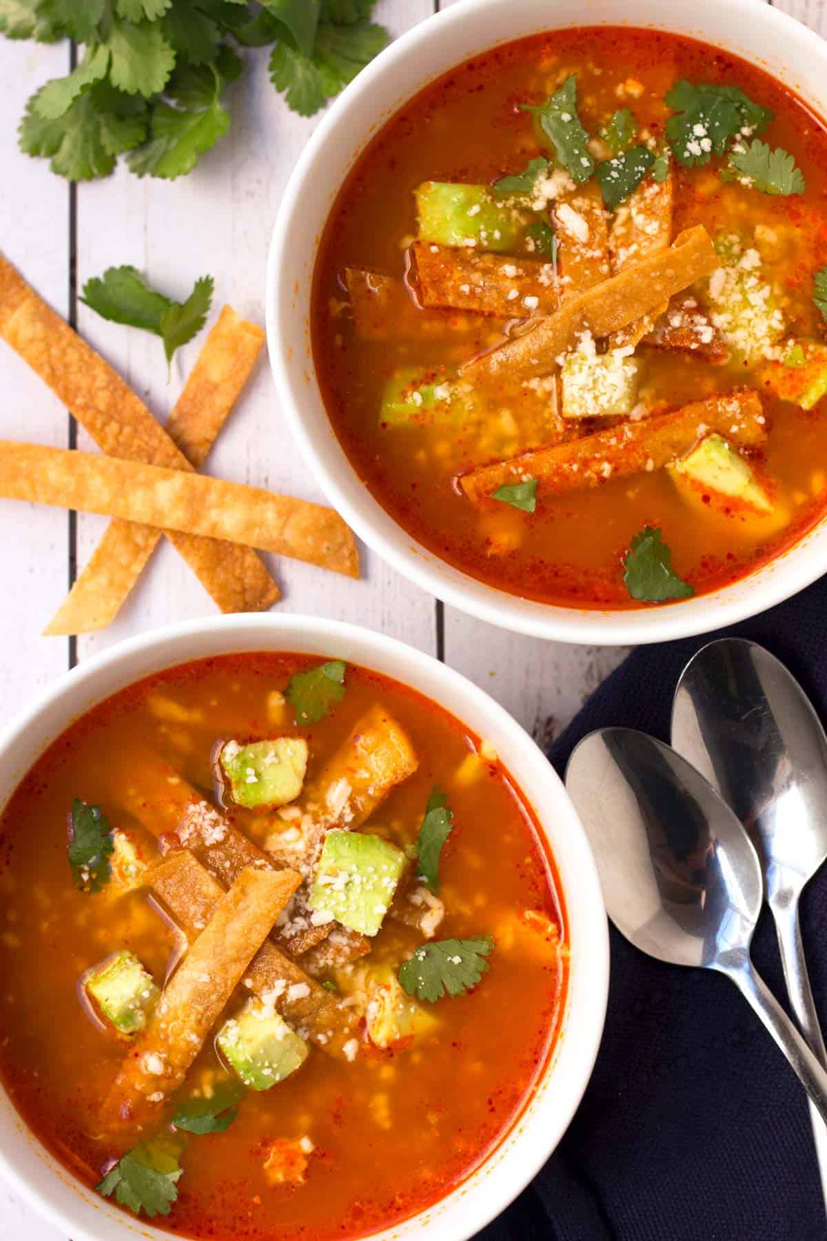 Mexican tortilla soup in bowls with spoons and toppings.