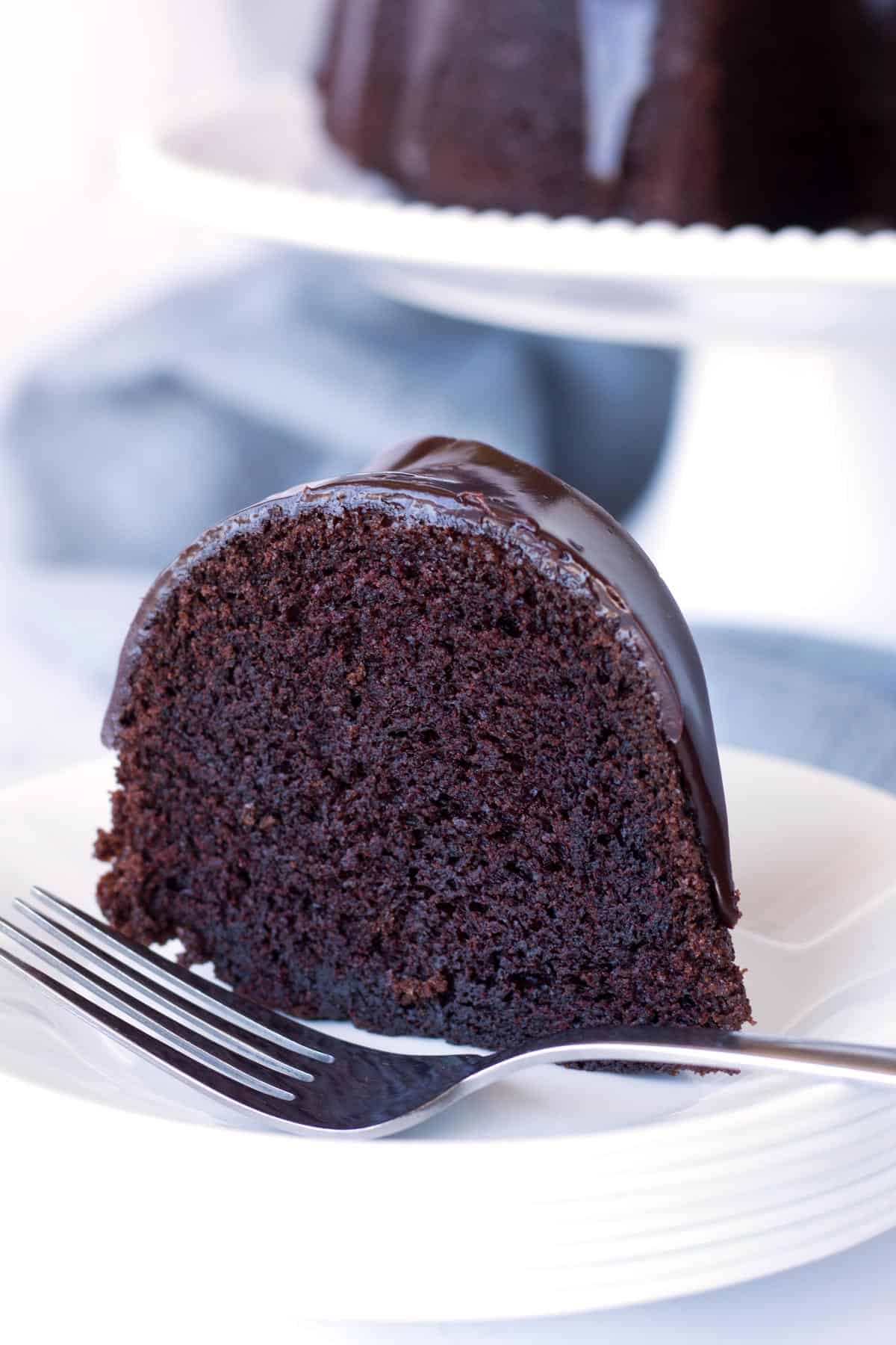 Slice of chocolate bundt cake on a stack of white plates with a silver fork sitting in front of the cake.