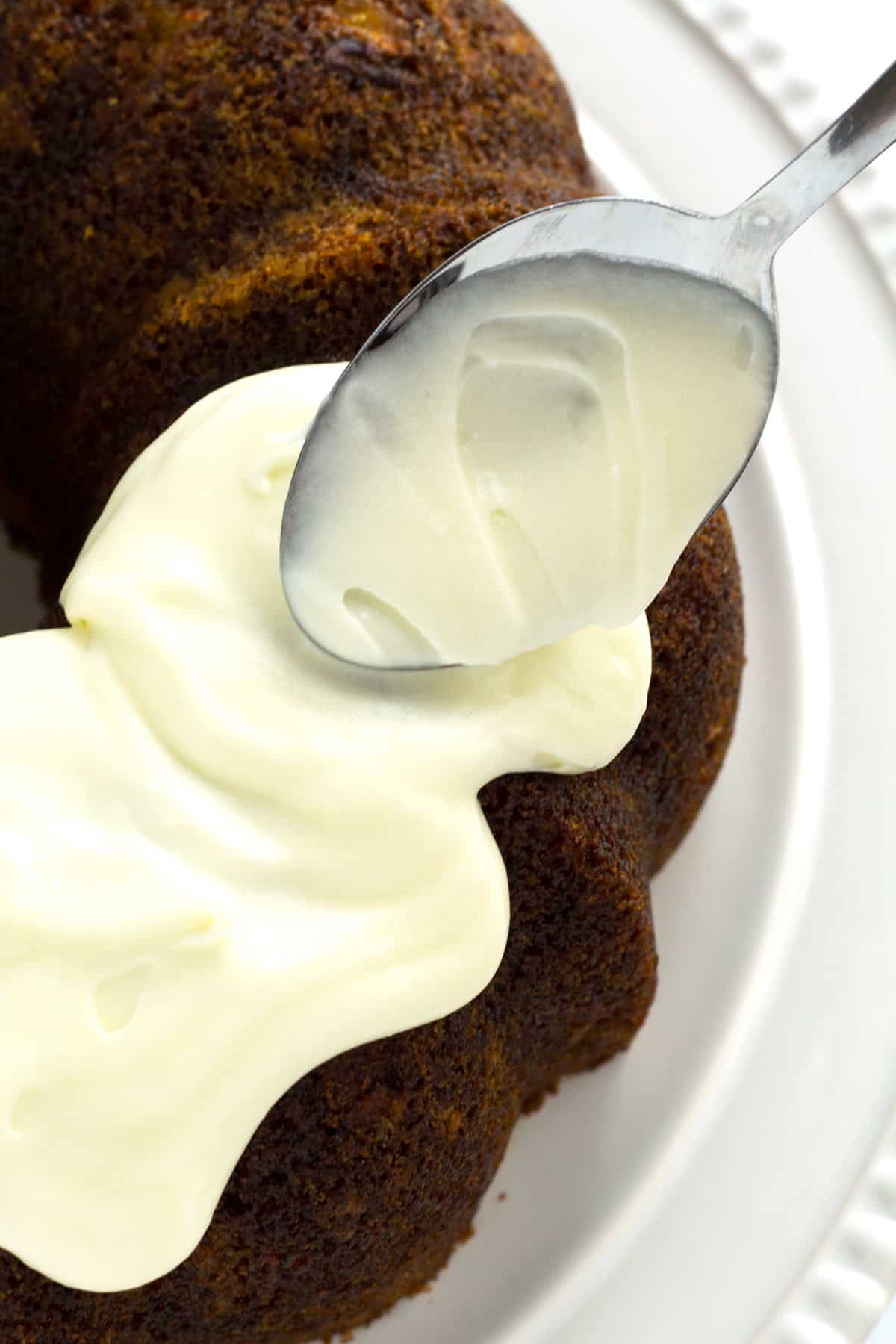 Spreading cream cheese frosting on carrot bundt cake with back of a spoon.
