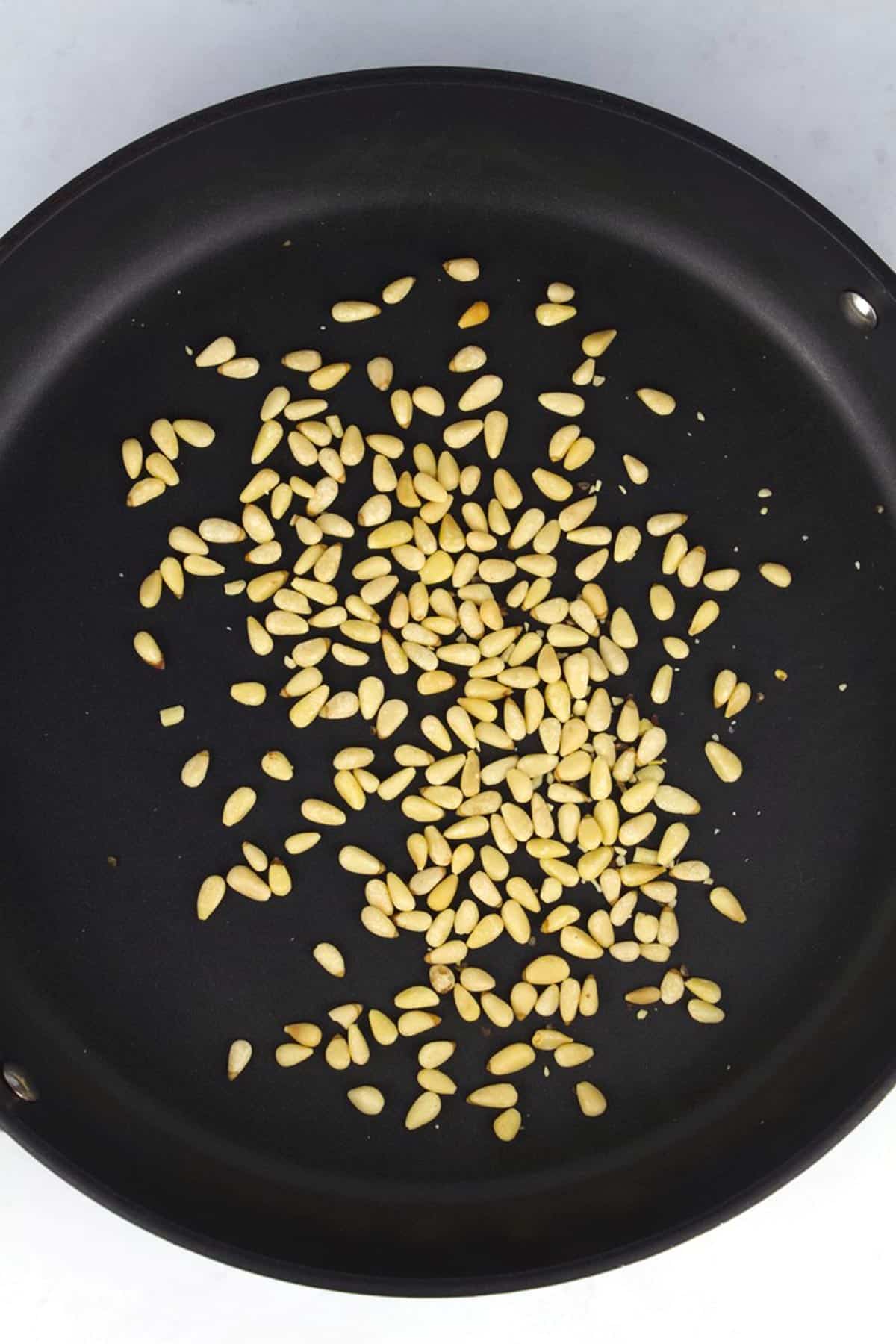 A black skillet with toasted pine nuts.