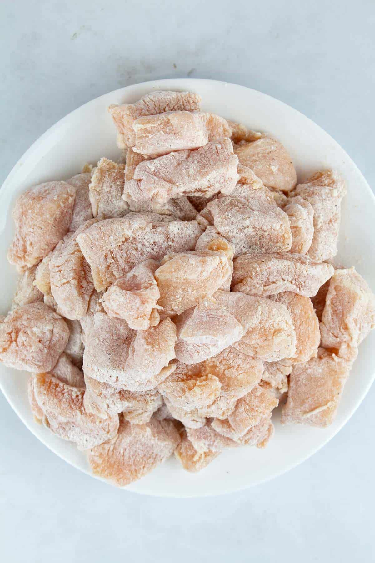 Lightly floured seasoned chicken breasts on a plate.