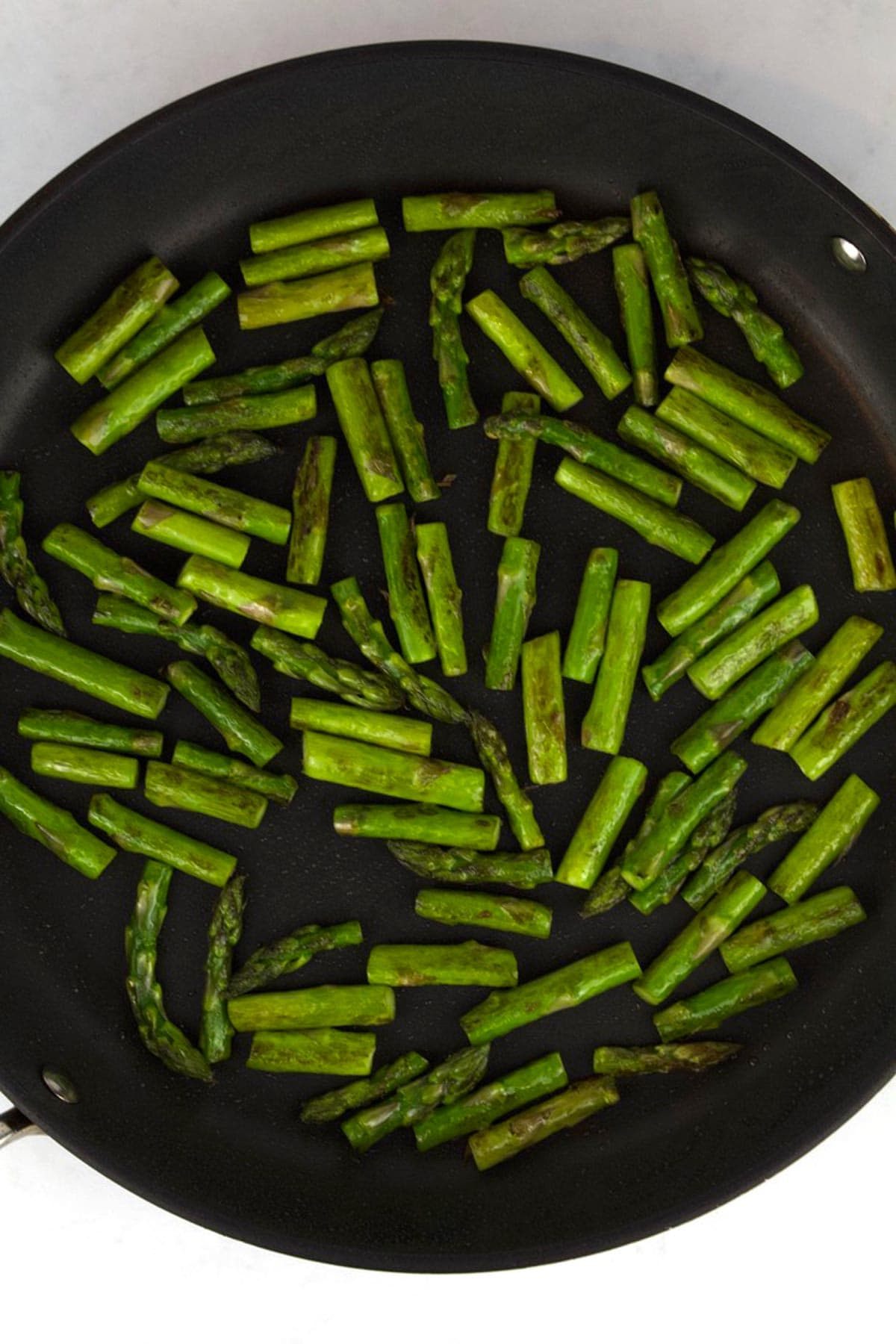 A black skillet with chopped, roasted asparagus.