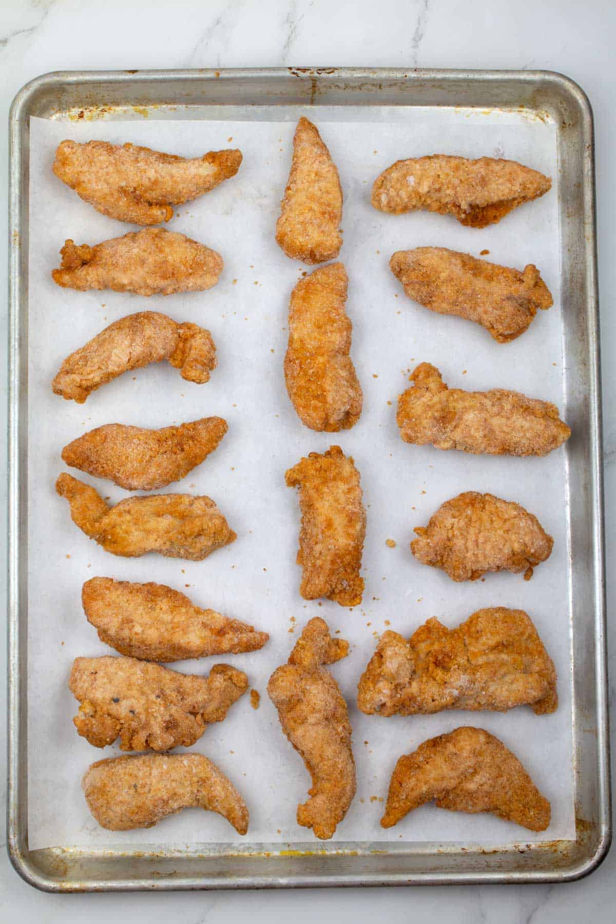 Chicken tenders on a parchment-lined baking sheet before cooking in oven.