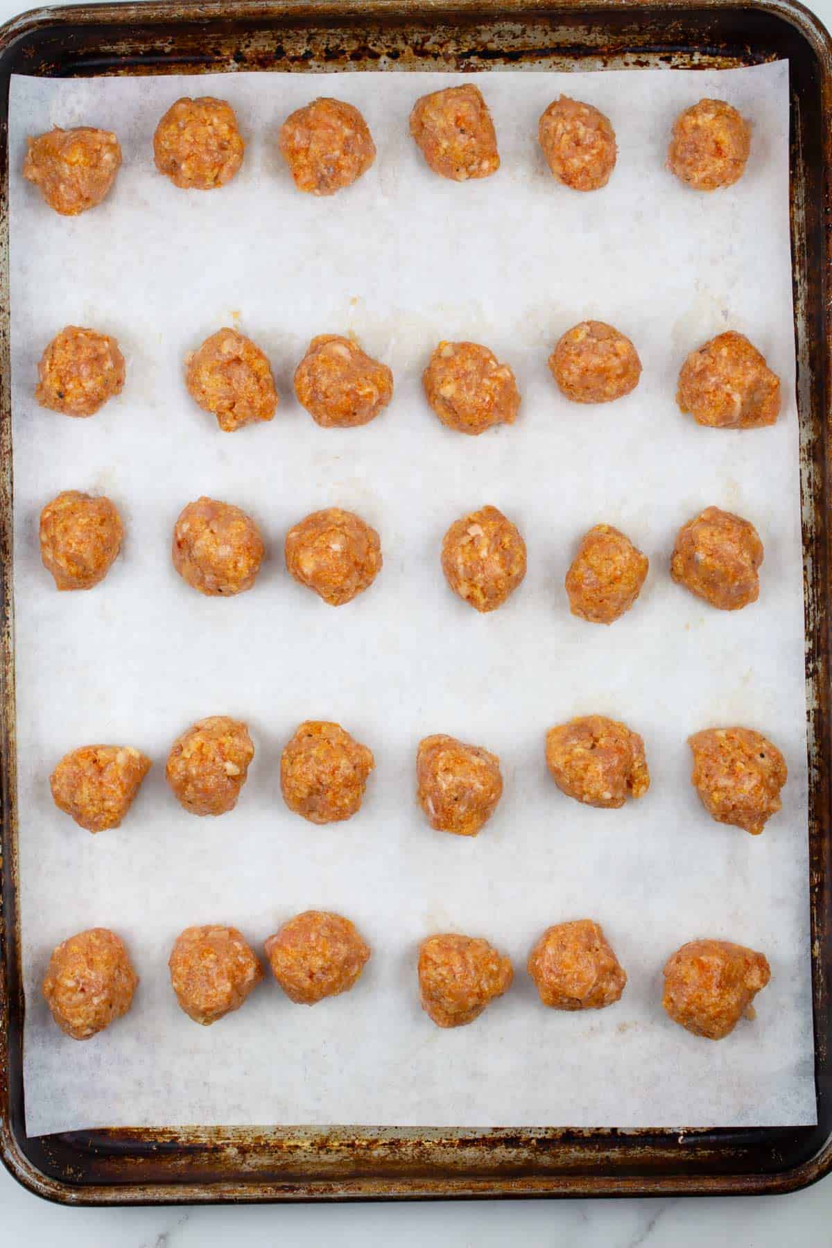 Raw meatballs rolled into balls and laid in rows on a lined cookie sheet.