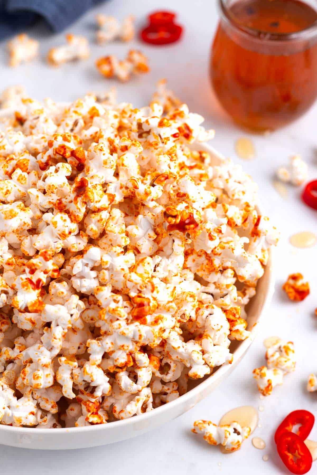 Spicy hot honey popcorn in a serving bowl with red fresno chili slices and honey drips on counter top.
