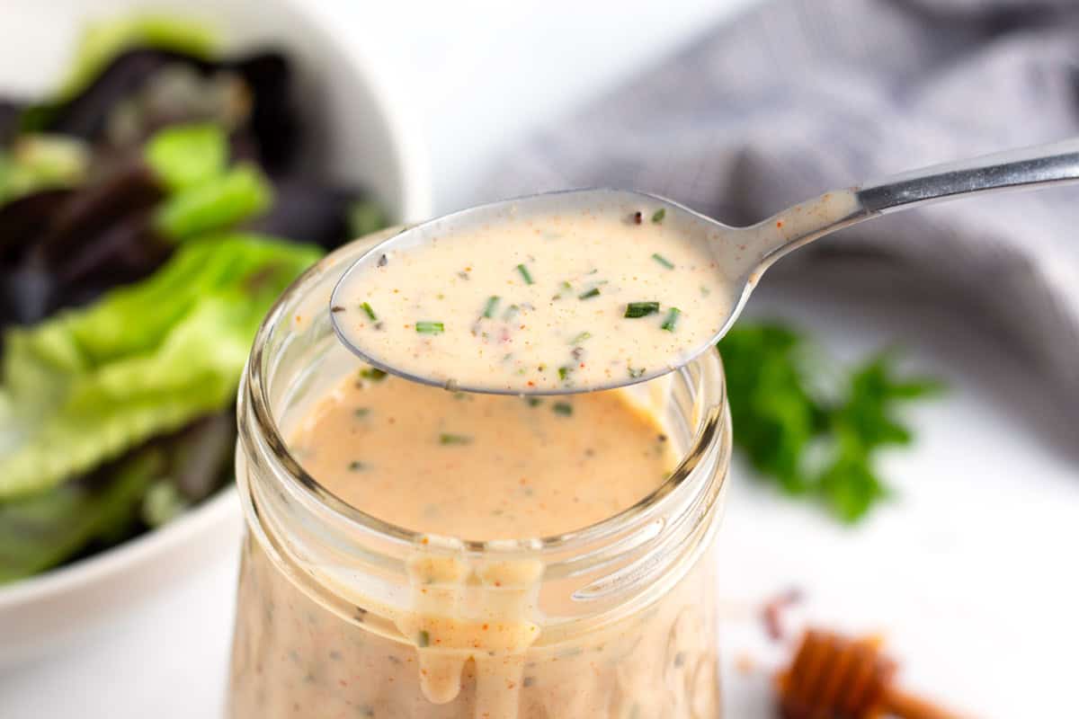 Spoon full of spicy ranch dressing filled with hot honey mixture with lettuce in the background.