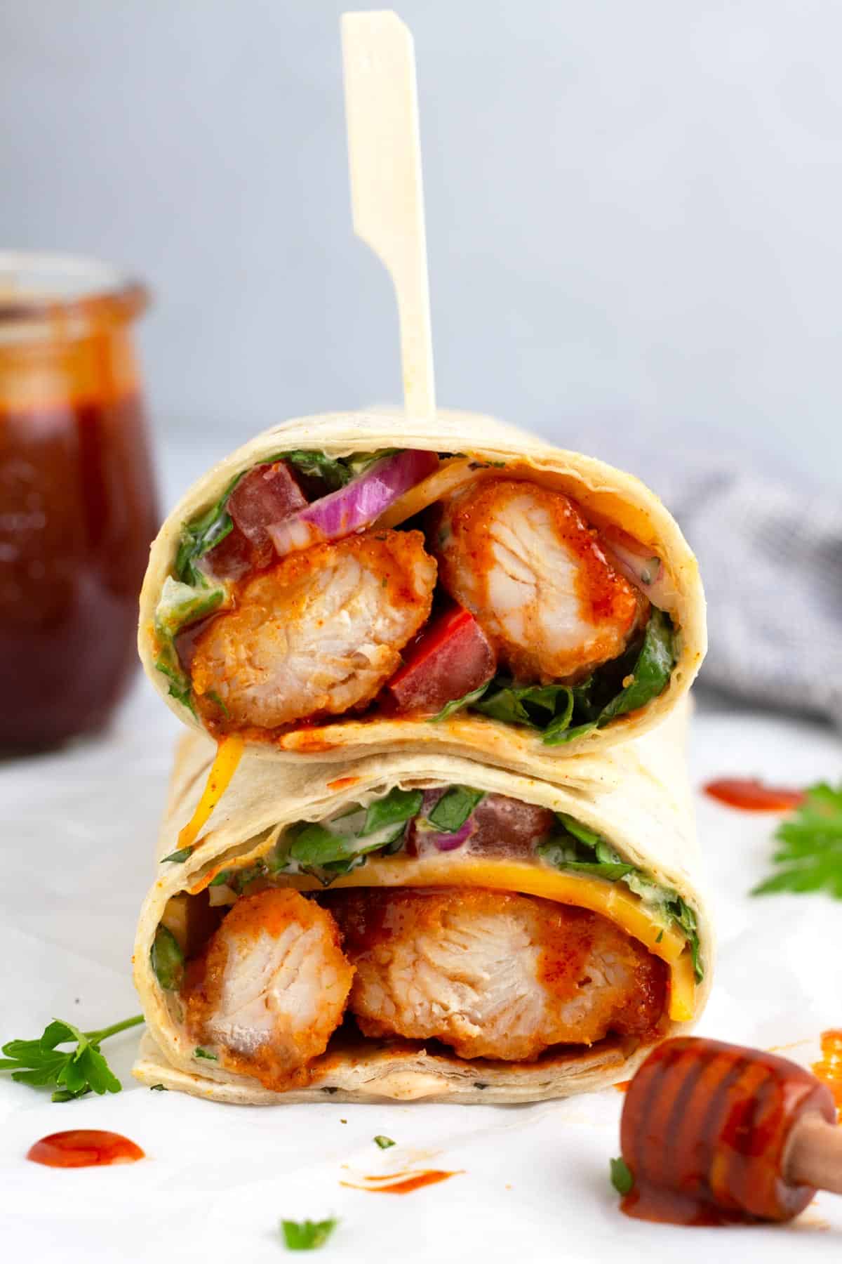 Chicken in a tortilla wrapped up with heat infused honey sauce dipped stick in the foreground.