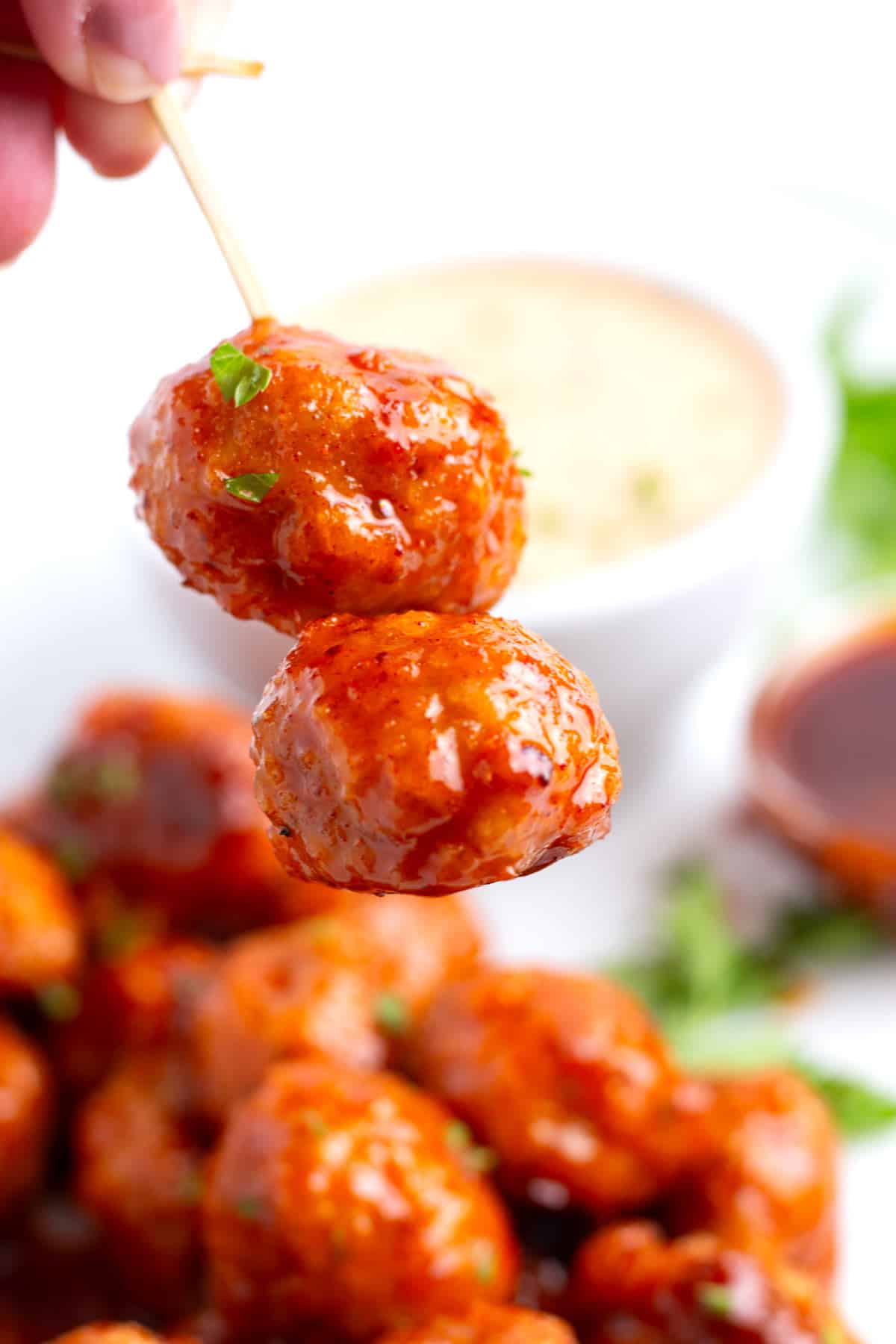 Two meatballs glazed in sweet and spicy sauce on a toothpick with more in the background.