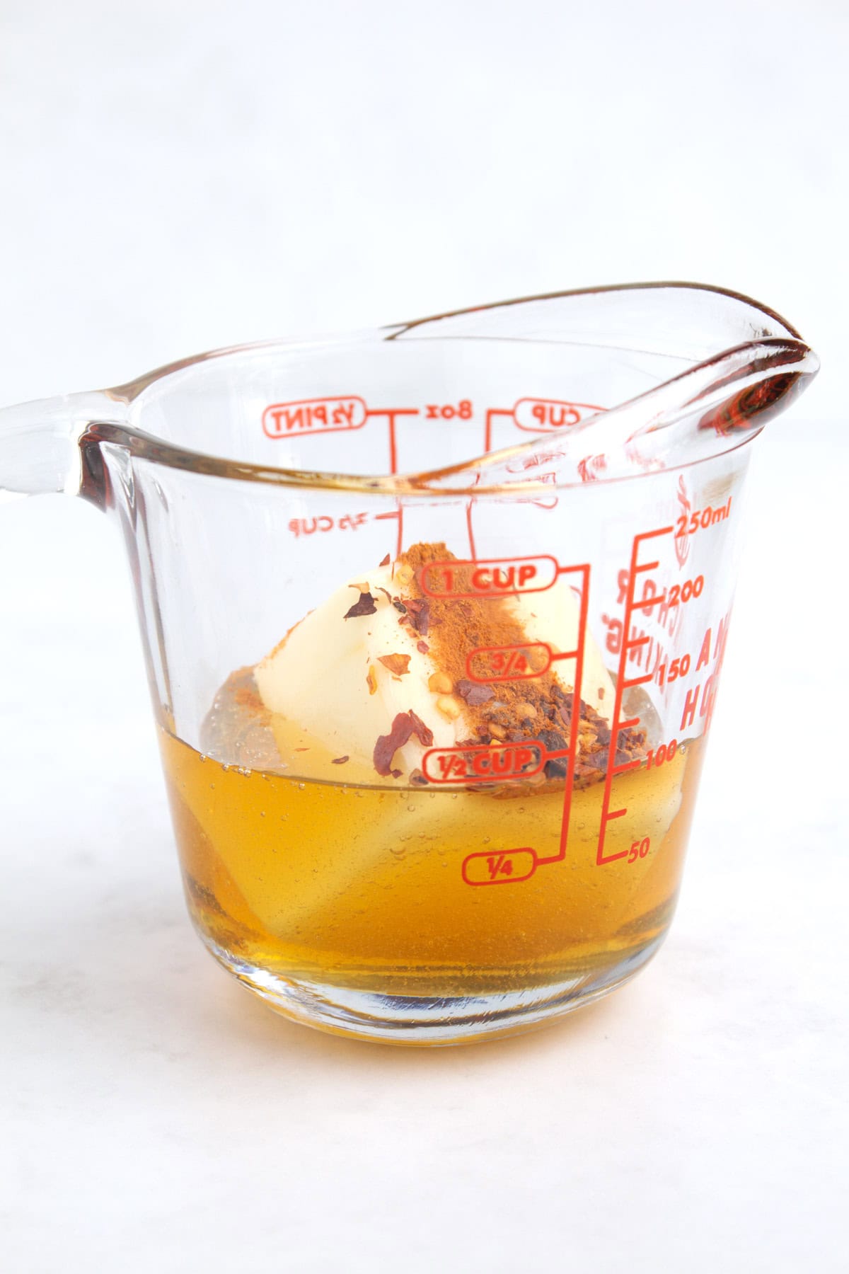 A 1 cup glass measuring container with honey on the bottom, a chunk of cold butter in the honey, and spices on top of the butter.