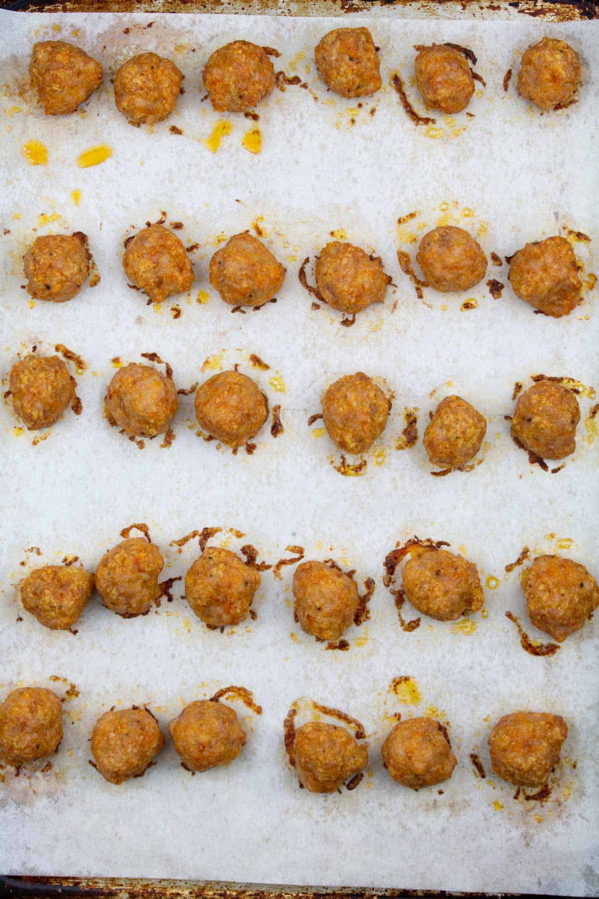 Juicy baked chicken meatballs after cooking in onion lined up on parchment-lined sheet pan.