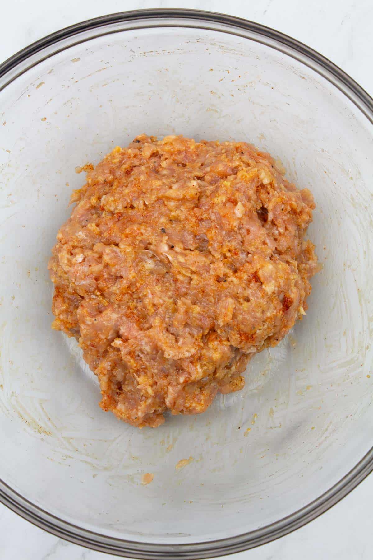 Ground chicken and other meatball ingredients mixed together in a bowl.