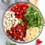 Pepperoni, bowtie pasta, arugula, cherry tomatoes, mozzarella pearls, and dressing layered in glass dish.