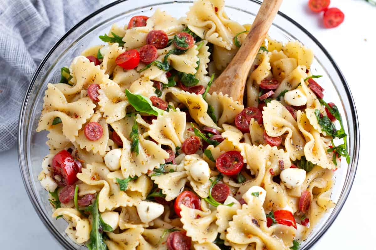 Serving spoon in bowl of spicy and sweet pasta salad with towel on the side.