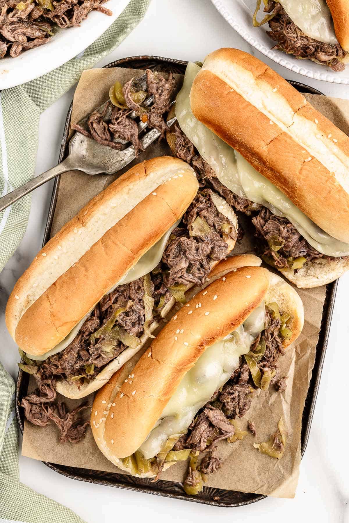 Overhead view of three sandwiches on a dark cookie sheet lined with parchment paper with a fork and extra food on the edges of the photos.