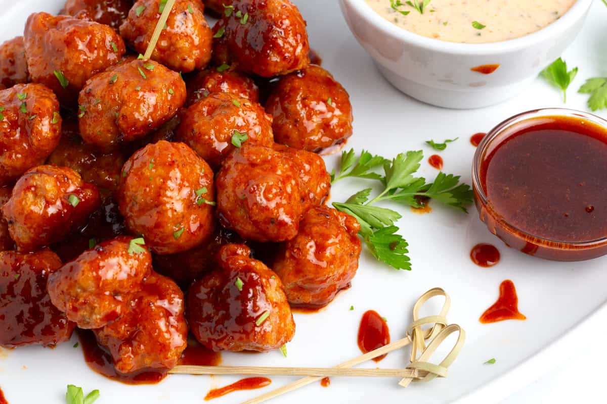 Tender meatballs on platter with cooling sauce and extra spicy honey sauce speckled with parsley flakes.