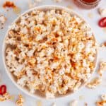 Bowl filled with sweet, spicy, and salty popcorn decorated with red chilis and drips of hot honey.