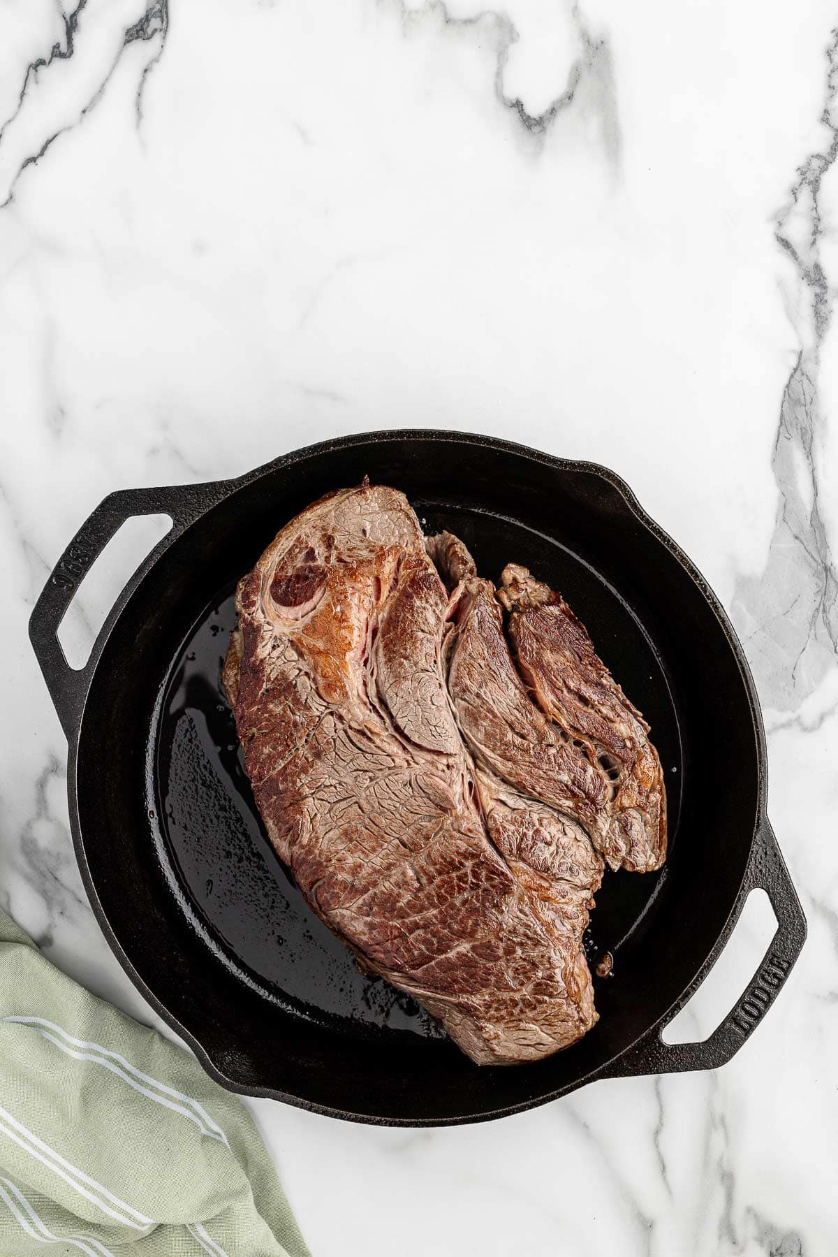 Overhead view of chuck roast being seared in a black cast iron skillet.