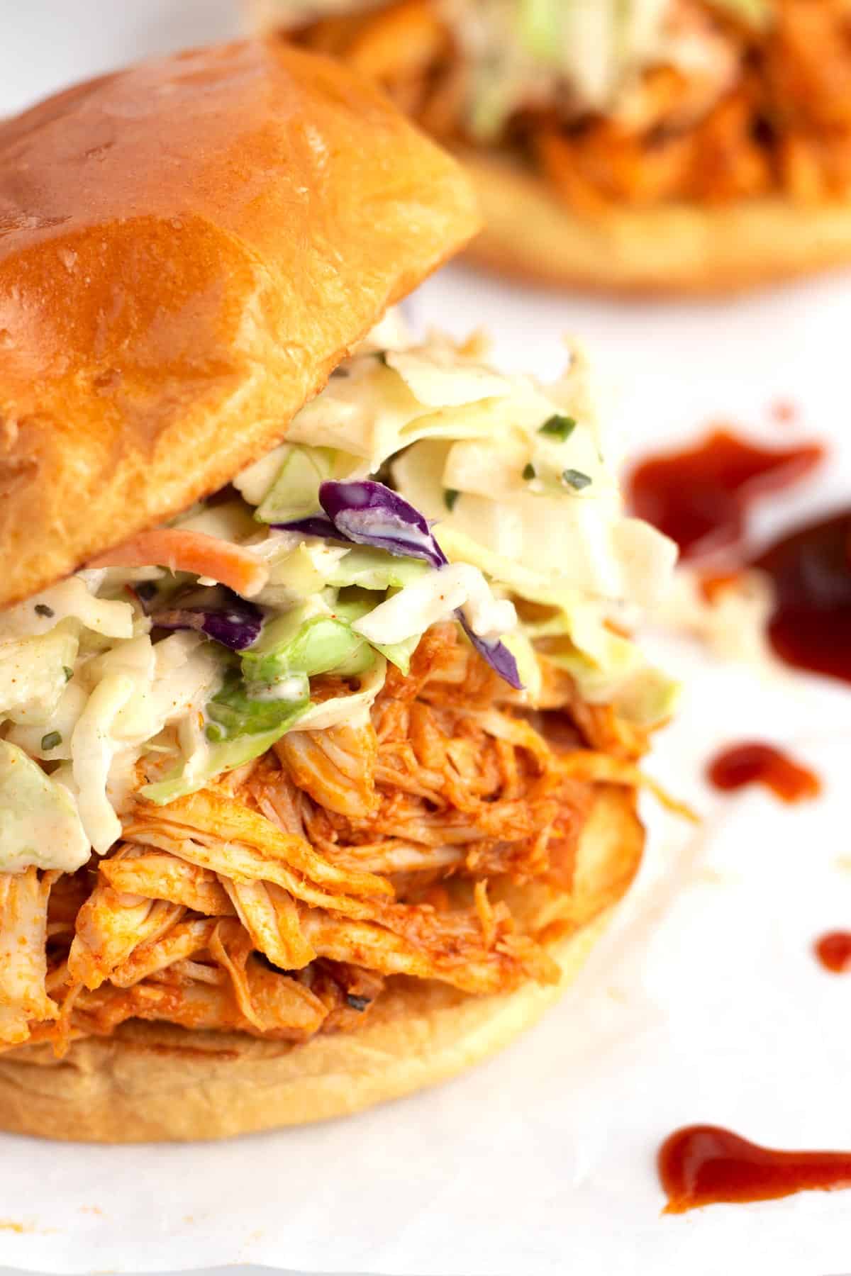 A super close view of a hot honey chicken sandwich with shredded chicken covered in red sauce, coleslaw, and a bun on top.