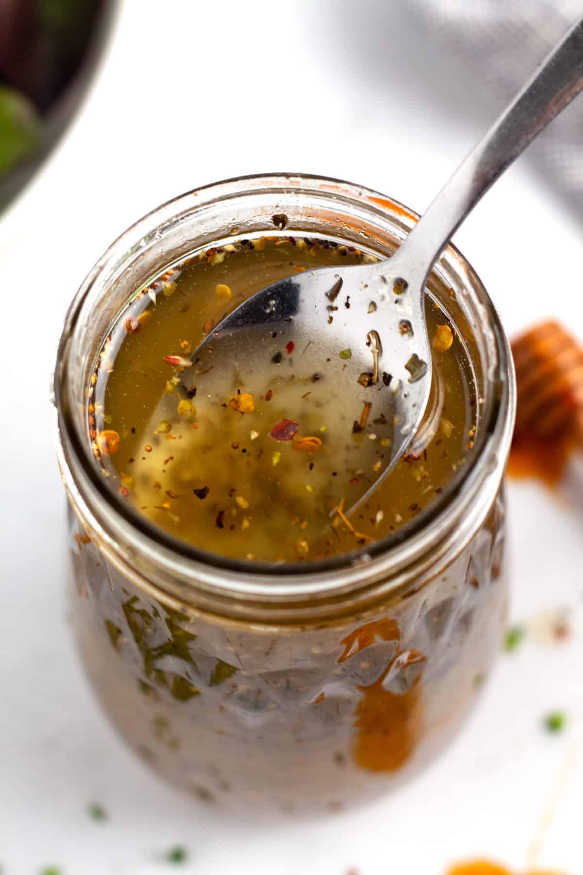 A close view of a spoon coming out of a jar of salad dressing.