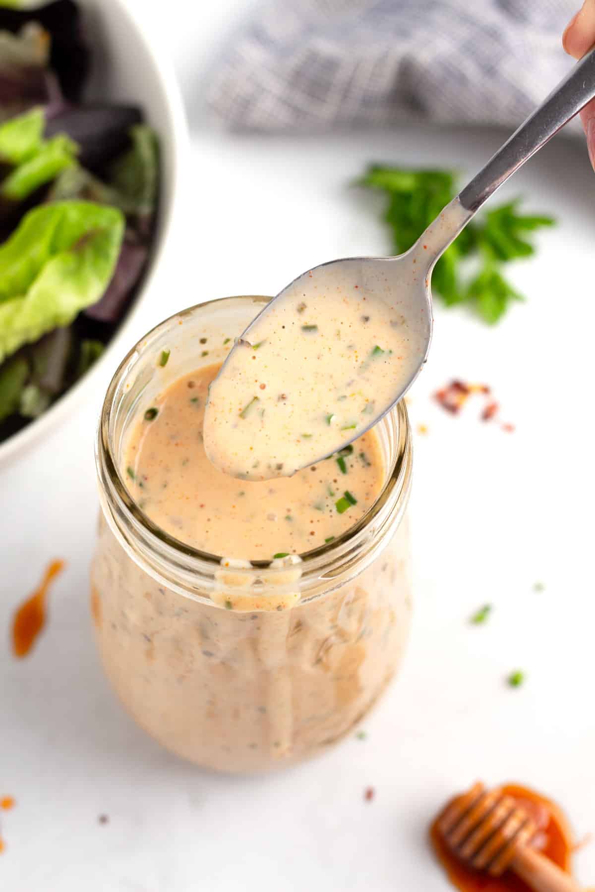 Spoonful of hot honey ranch sprinkled with cayenne pepper and chili flakes over a salad dressing jar.
