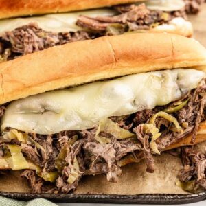 A sandwich with shredded chuck roast, pepperoncini, and melted cheese on a dark cookie sheet.