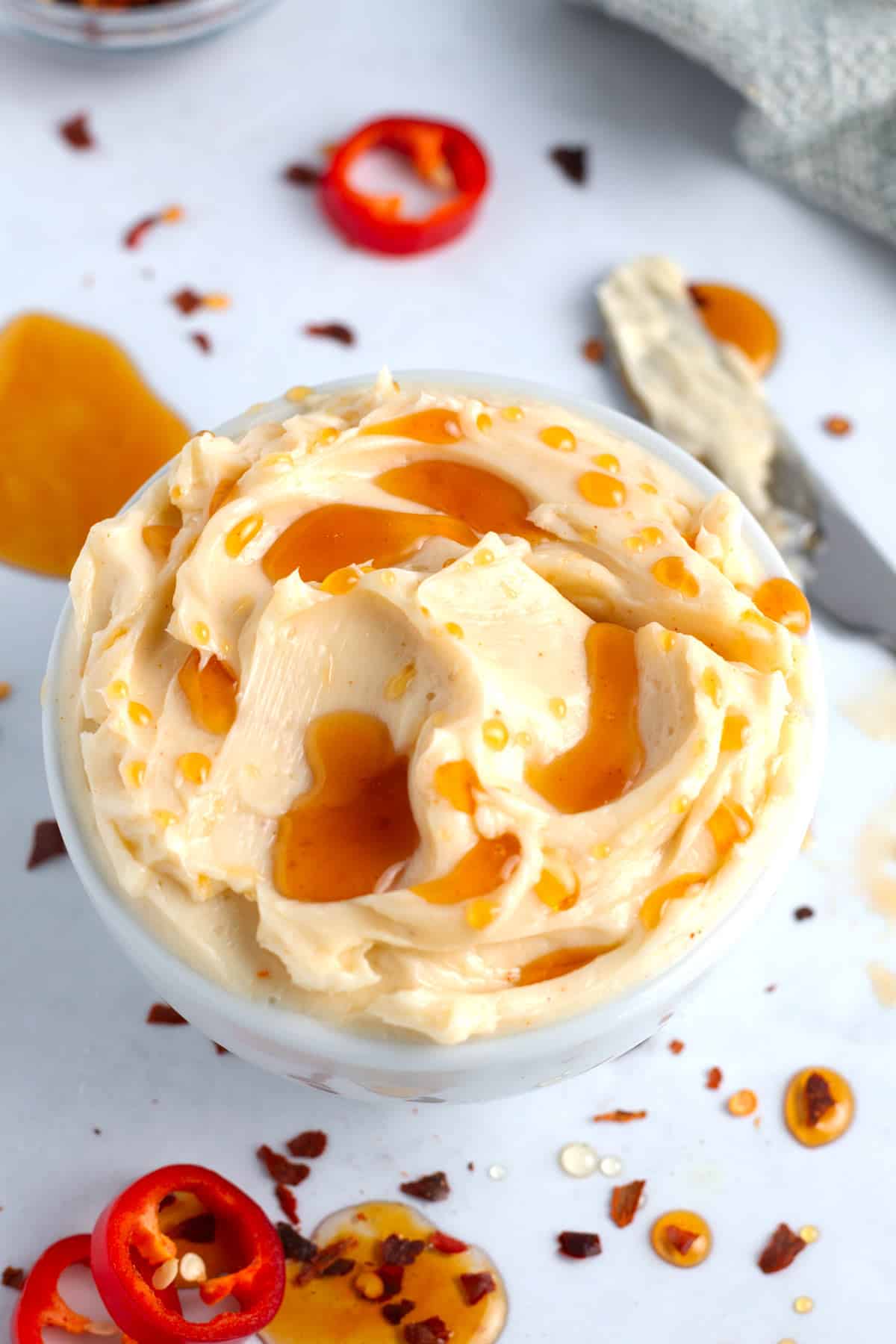 Butter that has been whipped with spicy honey in a white bowl sprinkled with ground cayenne pepper and chili flakes.