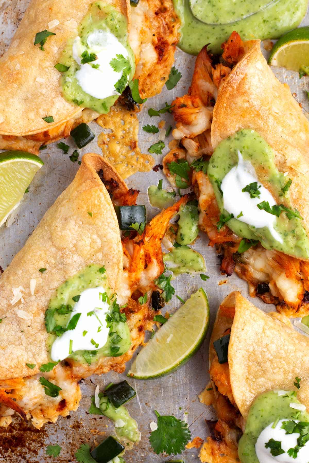 Overhead shot of four stuffed tortillas topped with green salsa, sprinkled with cilantro, and with lime wedges around the scene.