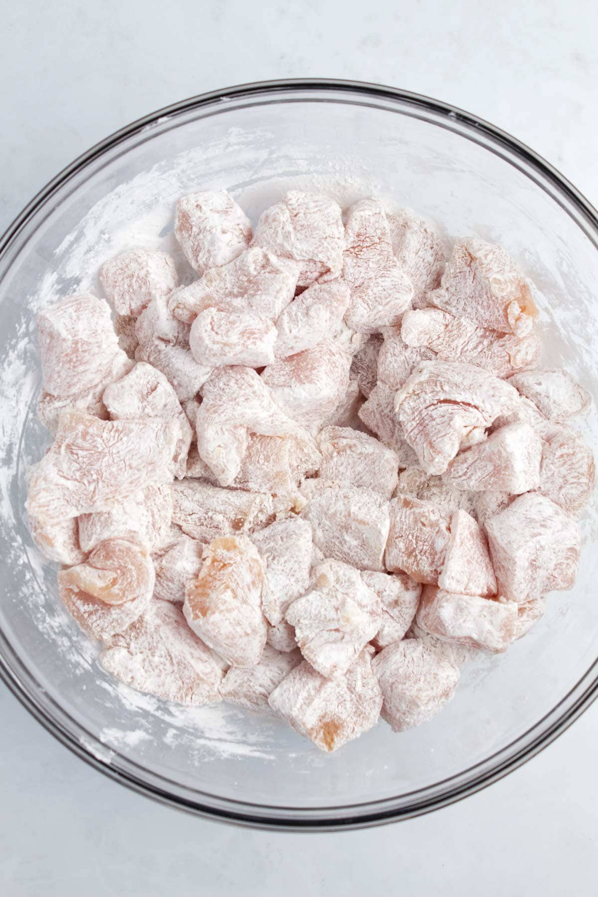 A glass bowl full of chicken cubes coated in cornstarch.