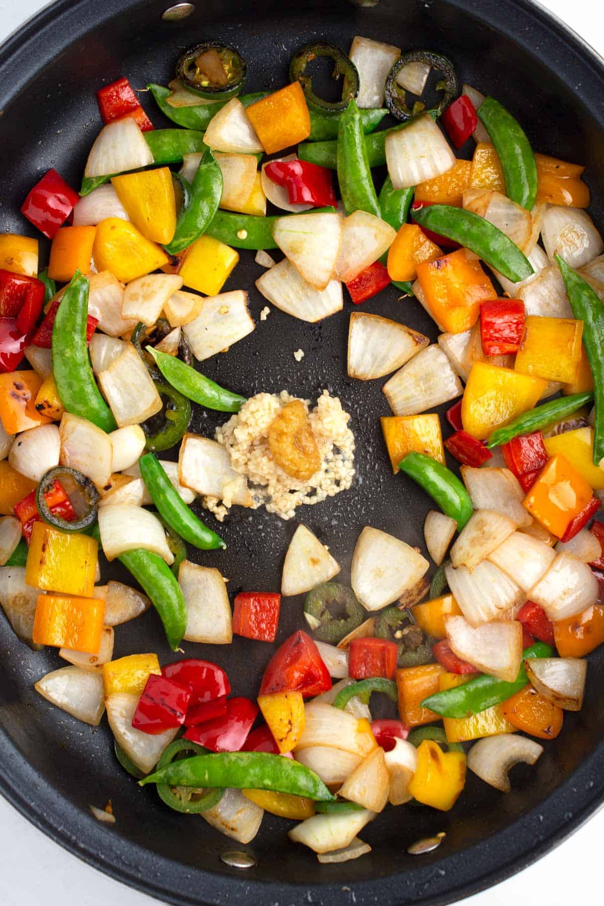 Veggies in a black skillet with garlic and ginger cooking in an empty spot in the middle.