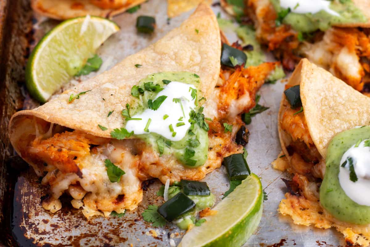 Crispy tortilla shells filled with chicken, cheese, and salsas on a gray baking sheet.