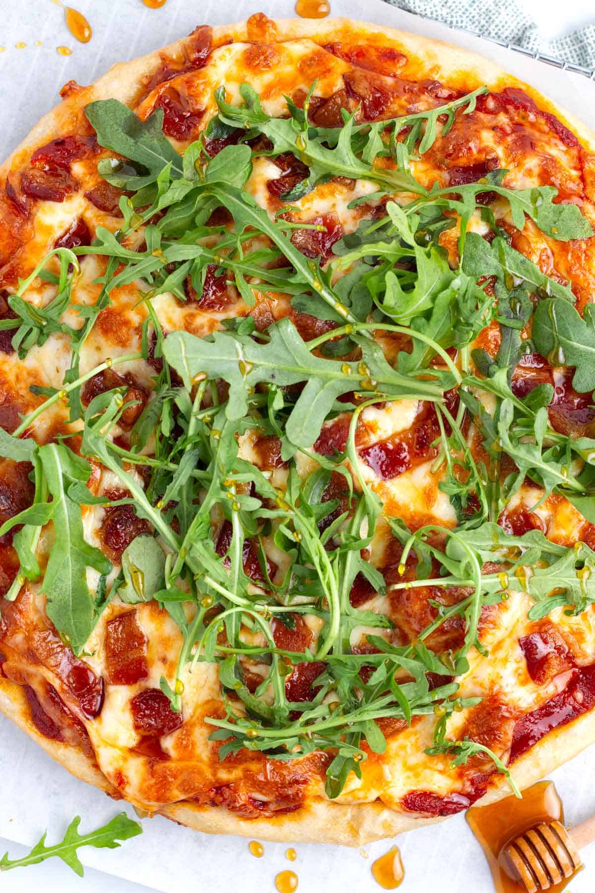 Hot honey drizzled over cast iron pizza topped with bacon and arugula after baking.
