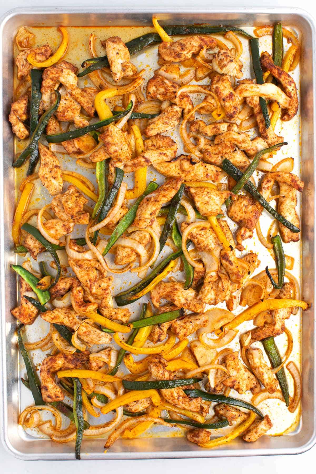 Cooked sliced chicken and peppers on a large silver baking sheet.