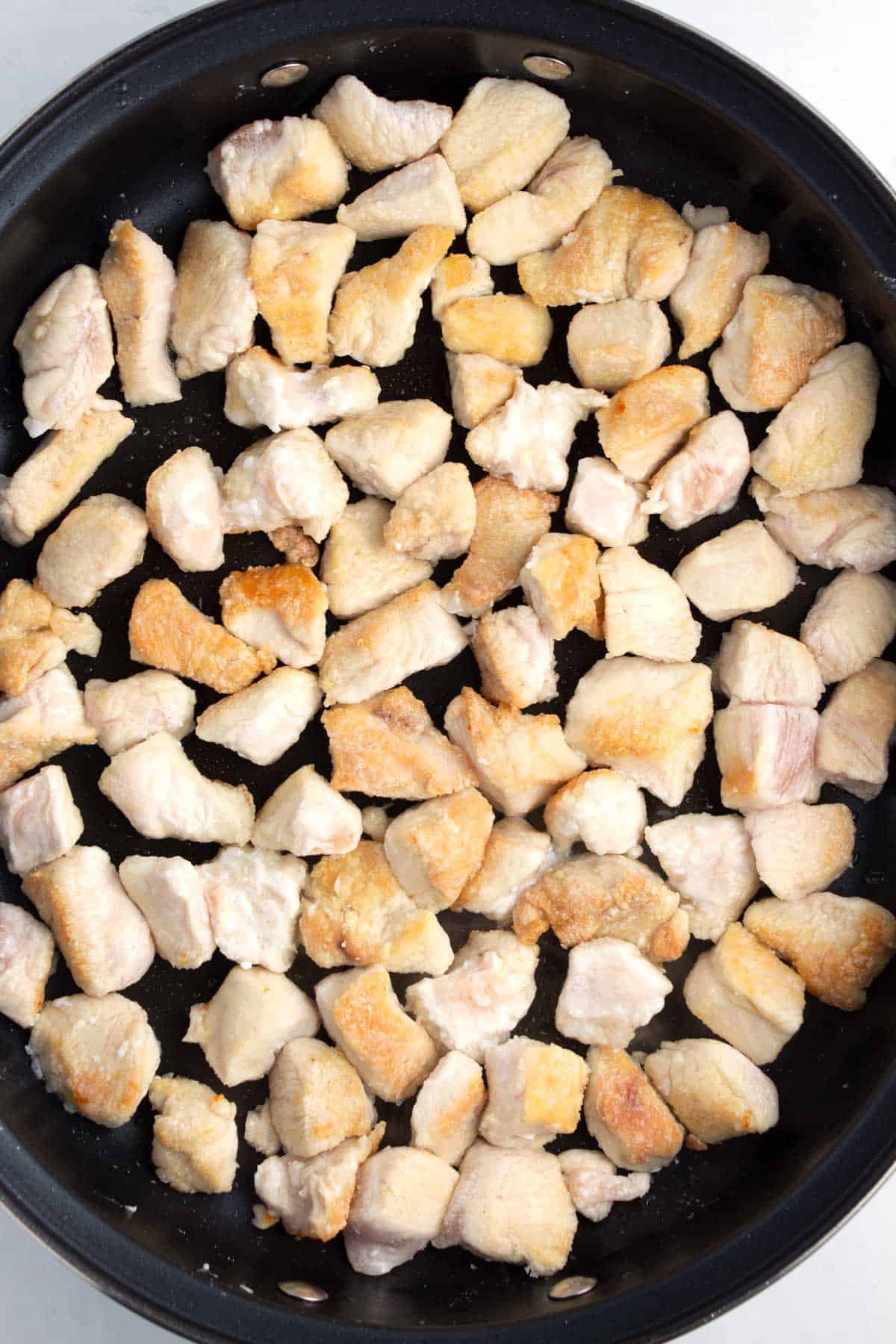 Lightly golden brown chicken cooking in a black skillet.