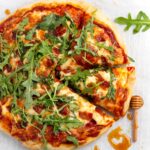Hot honey pizza on parchment paper topped with arugula and bacon pieces.