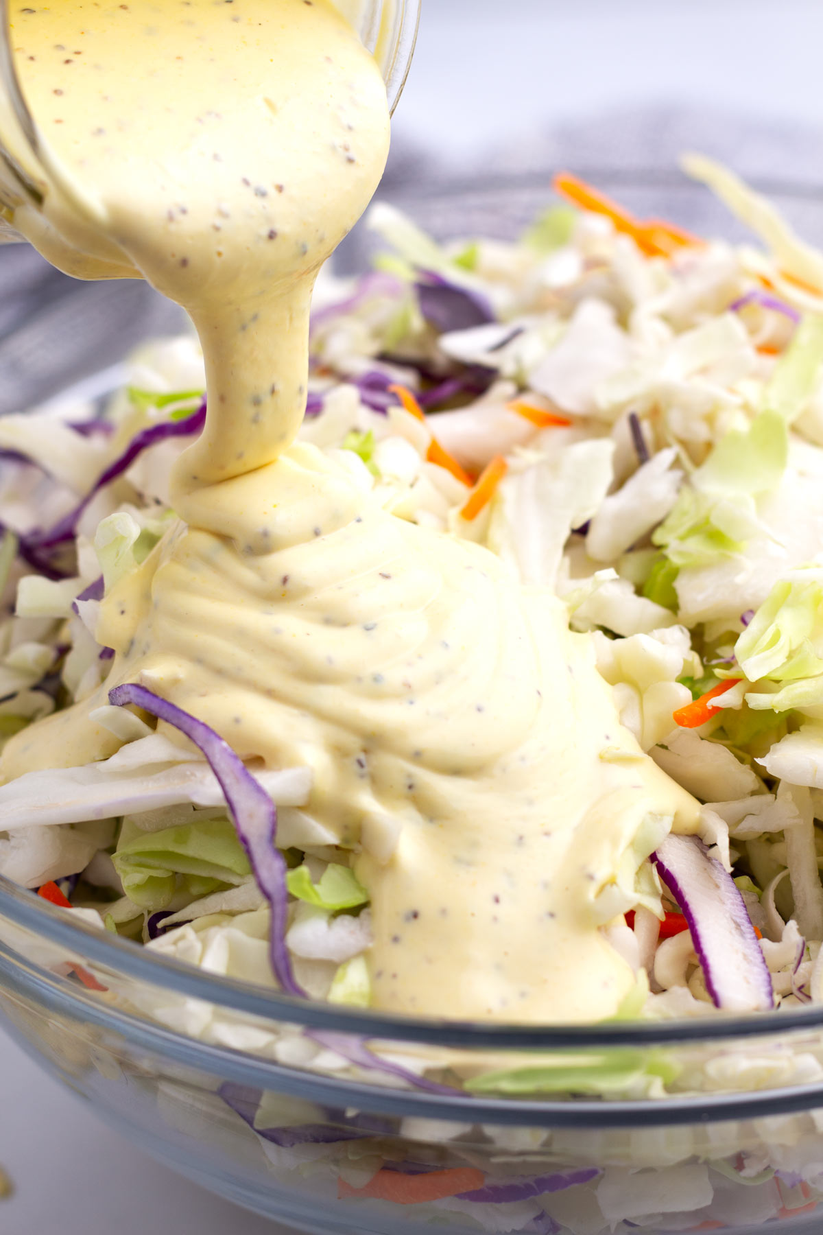 Jar with thick amount of dressing pouring over the top of bagged coleslaw mix.