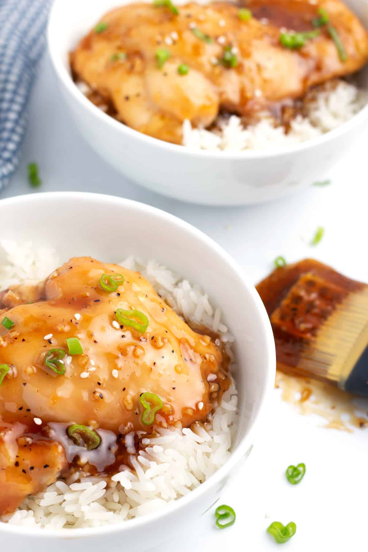 Two bowls of rice and glazed thighs with a silicone brush covered in sauce next to the bowls.