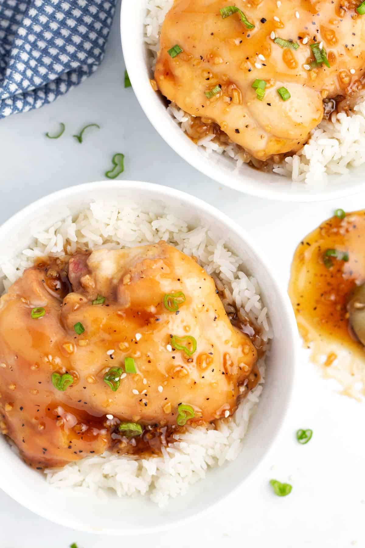 Two white bowls with rice and pieces of glazed chicken with a blue towel in the upper left hand corner.