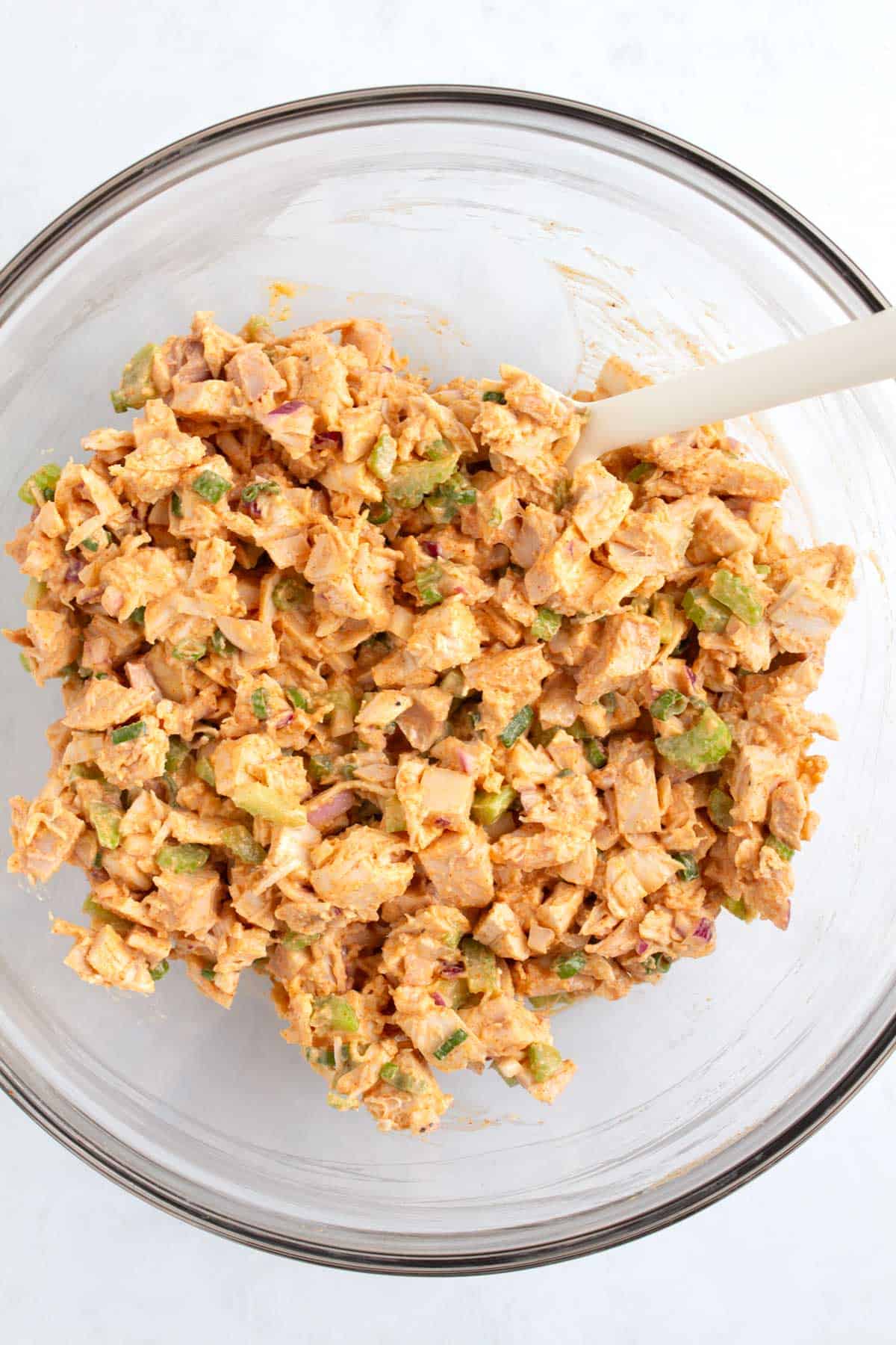 Chicken salad ingredients including hot honey yogurt mixture in a bowl and mixed together with spoon.