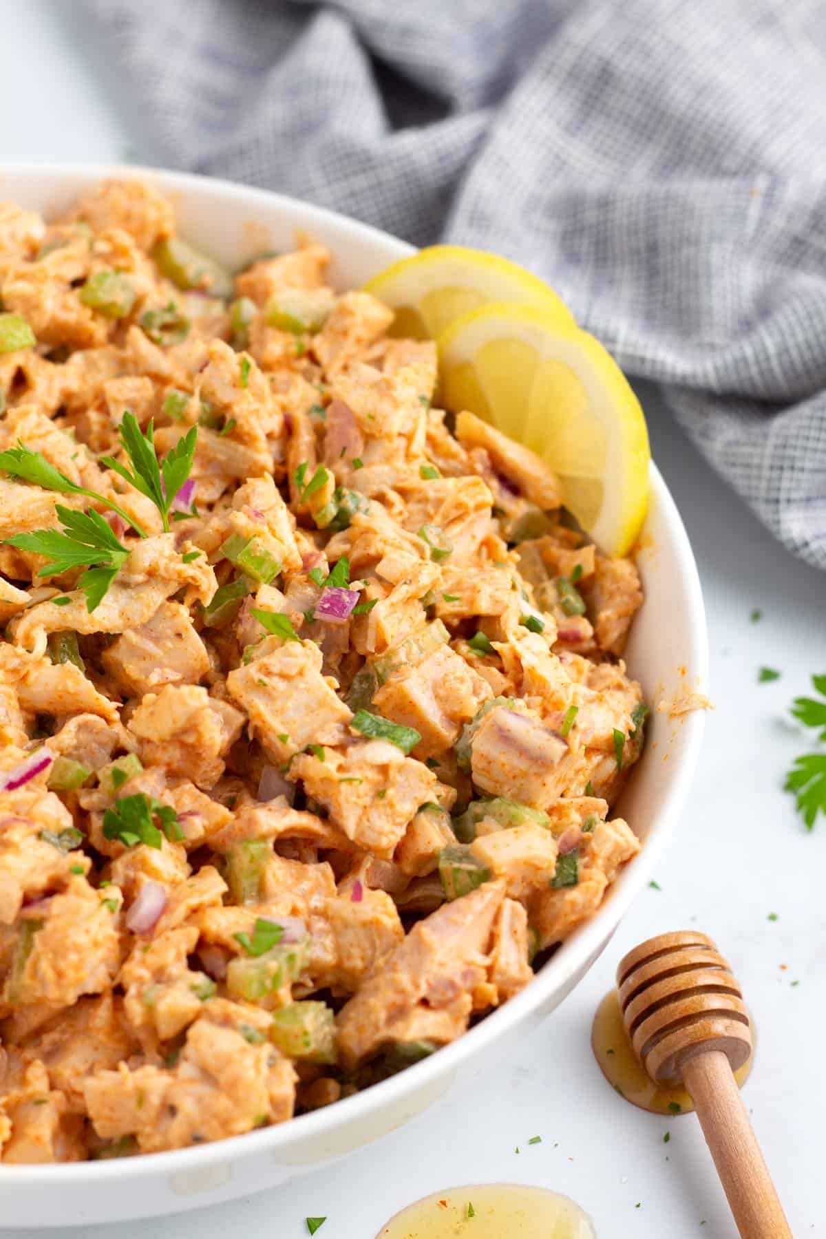 Chunks of chicken mixed together with chicken salad dressing and hot honey in a white bowl.