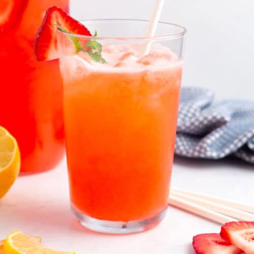 Lemon and strawberries on countertop with pitcher and glass of refreshing fresh, easy strawberry lemonade.