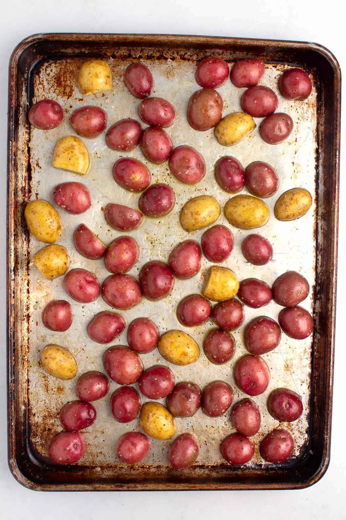 Putting baby potatoes with seasonings and oil on sheet pan.