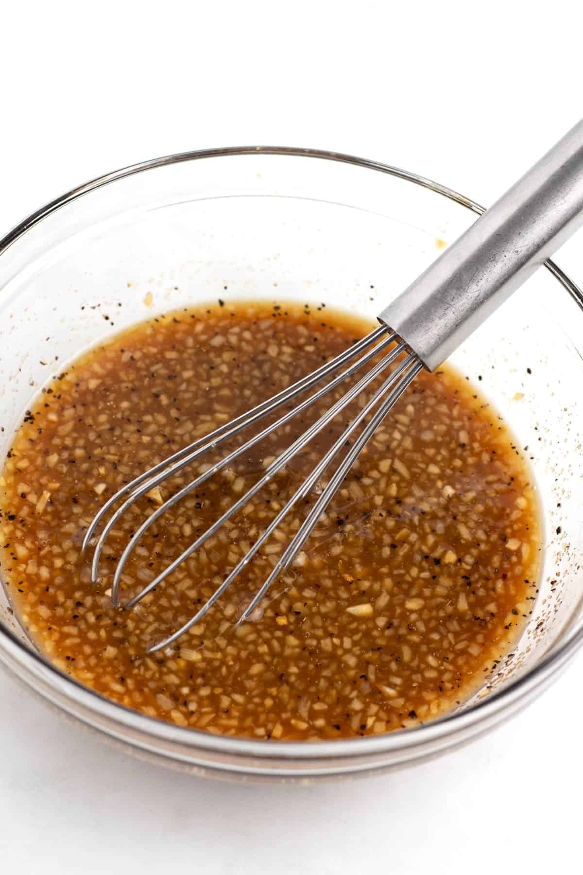 A bowl of brown sauce with lots of garlic and whisk sitting in the bowl.