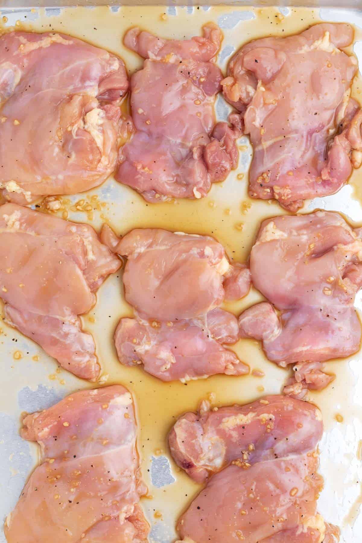 Raw meat coated in sauce and spread out on a silver baking pan.