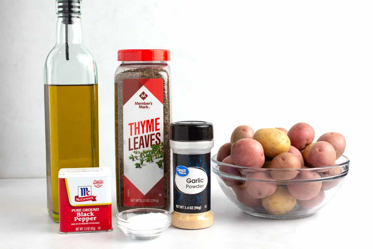 Olive oil, salt, pepper, thyme, garlic powder, and small potatoes on kitchen counter.