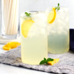 Lemons and mint on a cloth with two glasses filled with ice cubes and simple lemonade.