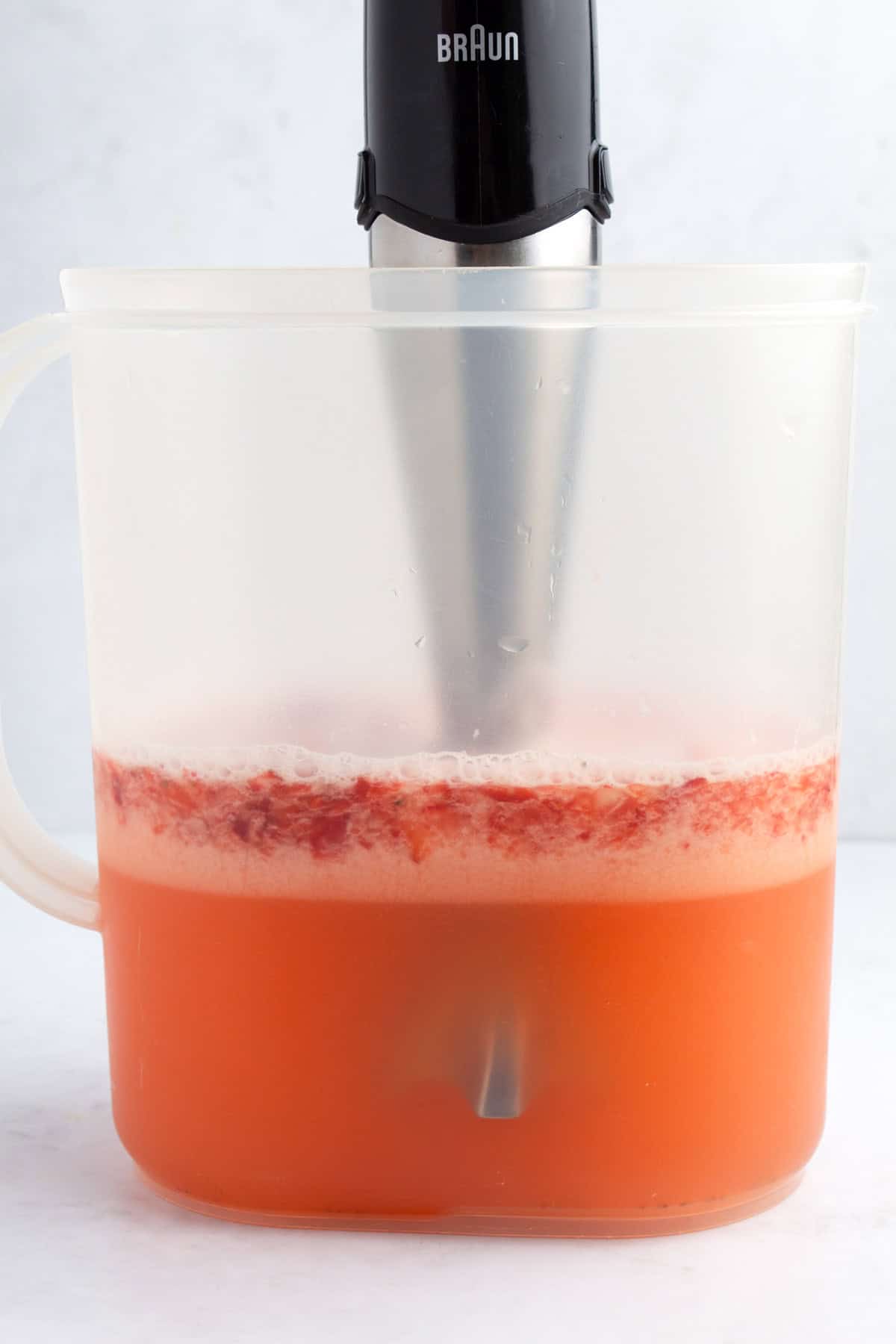 Pitcher filled with lemonade and strawberries being blended with an immersion blender.