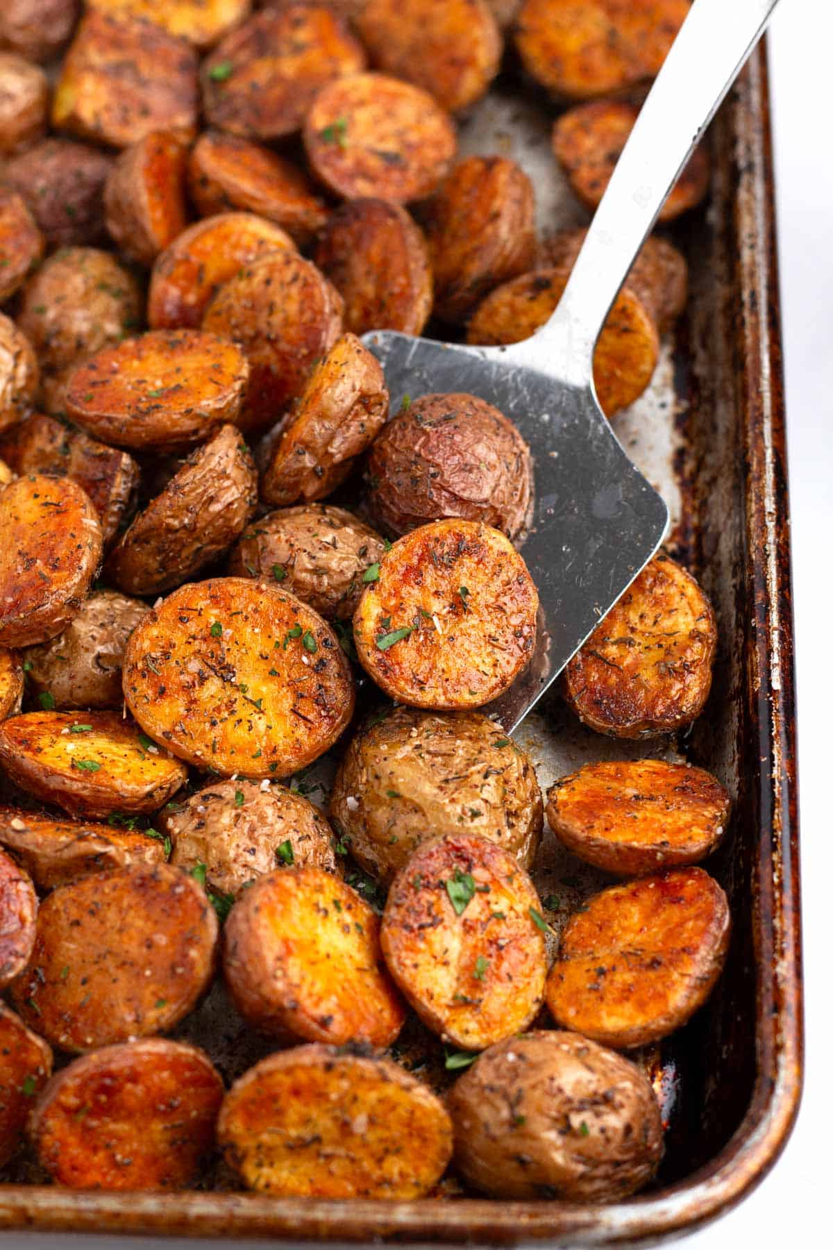 Spatula lifting crunchy oven roasted potatoes off sheet pan.