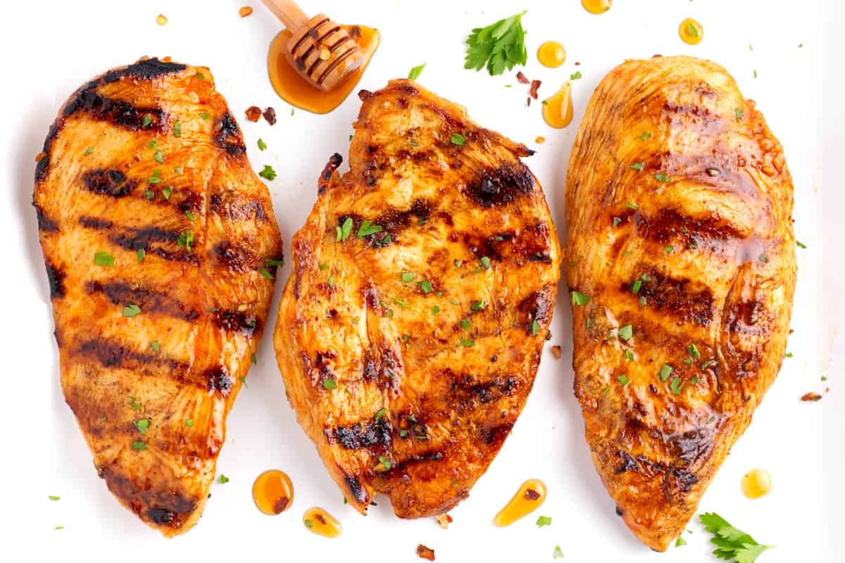 Plate with dollops of spicy honey and parsley with three grilled chicken breasts.